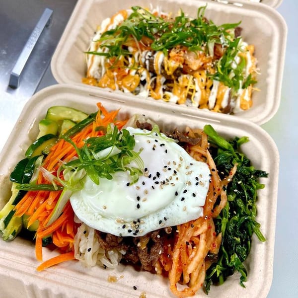 Two Korean bibimbap bowls in takeout containers, one topped with a fried egg and vegetables.