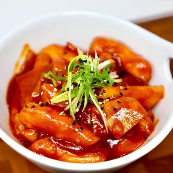 A white bowl filled with Korean tteokbokki, garnished with green onions and sesame seeds.