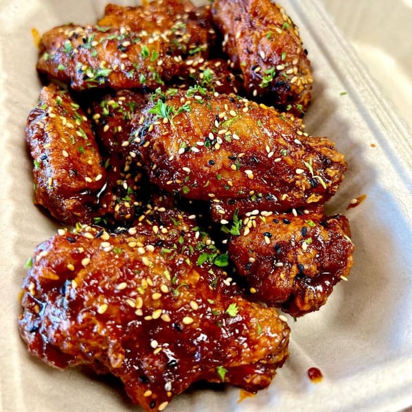 Close-up of Frymazing's Korean fried chicken wings, glazed with sauce, sesame seeds, and parsley.