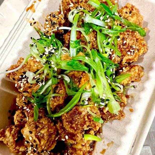 Crispy Korean fried chicken, drizzled with sauce, topped with green onions and sesame seeds.